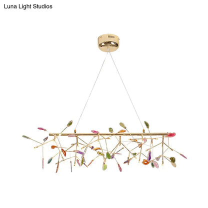 A modern gold-toned dining room ceiling light with colorful glass leaves on delicate branch bulb bases