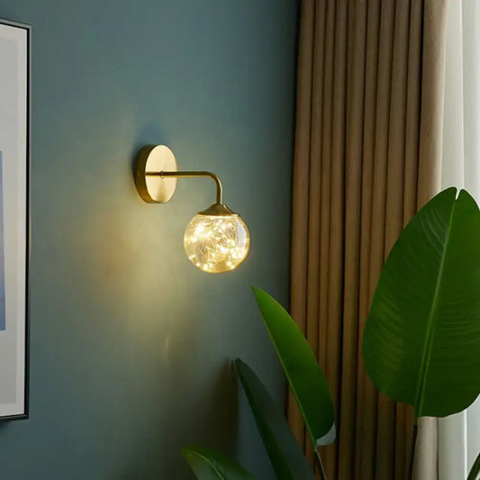 Nordic gold glass globe wall sconce featuring a gold-toned frame with warm fairy lights for bedroom decor