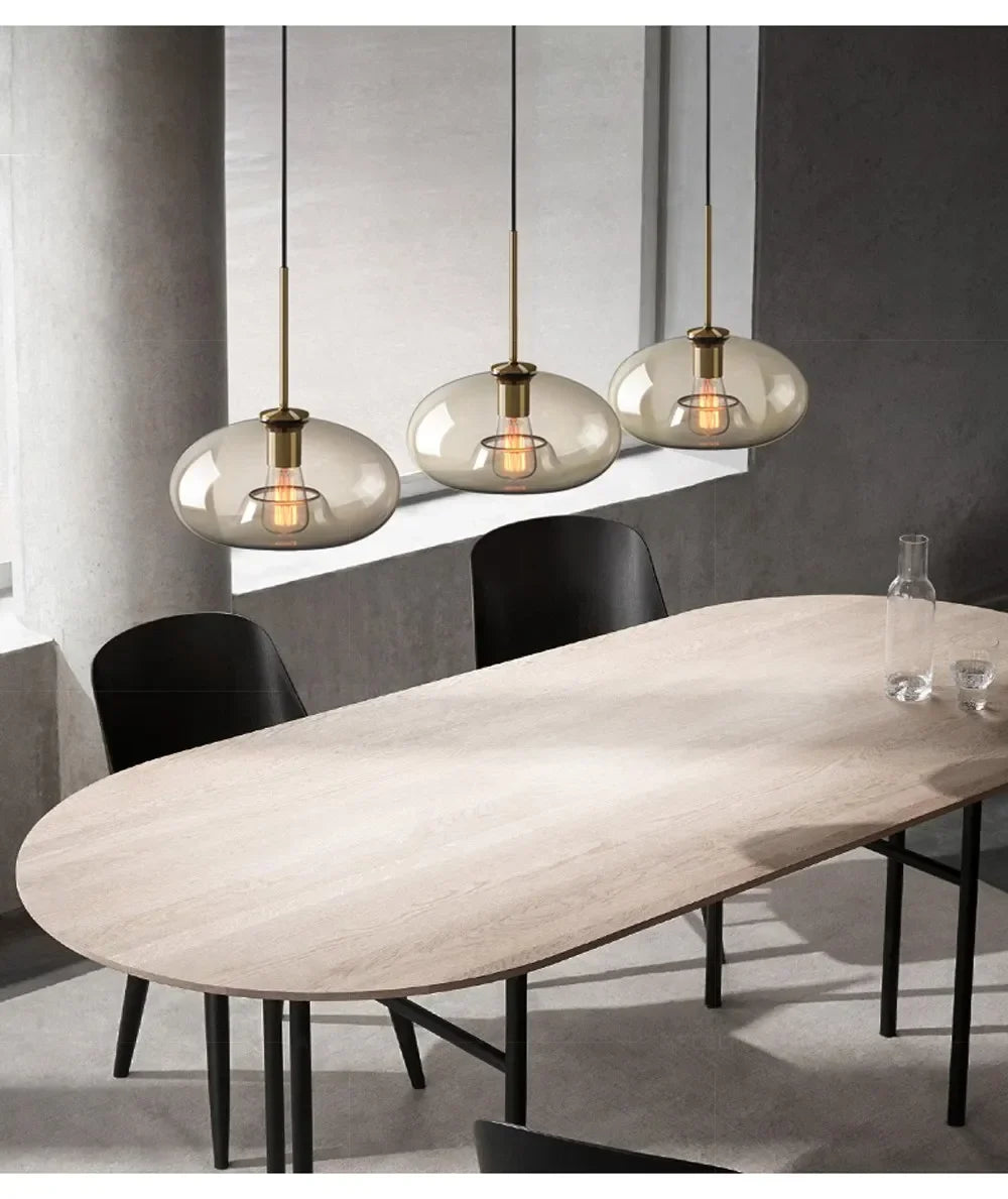 Three modern nordic led glass pendant lights with smoked glass globes and brass accents hang above a dining room table