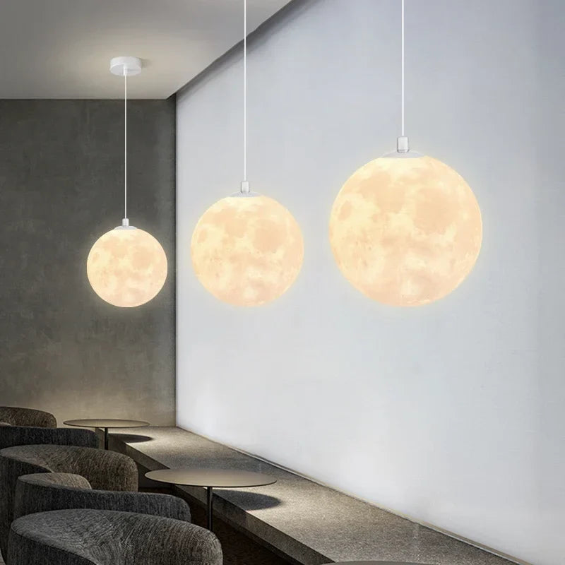 Three spherical nordic led moon pendant chandeliers with detailed craters hanging by white cords for dining room kitchen lighting