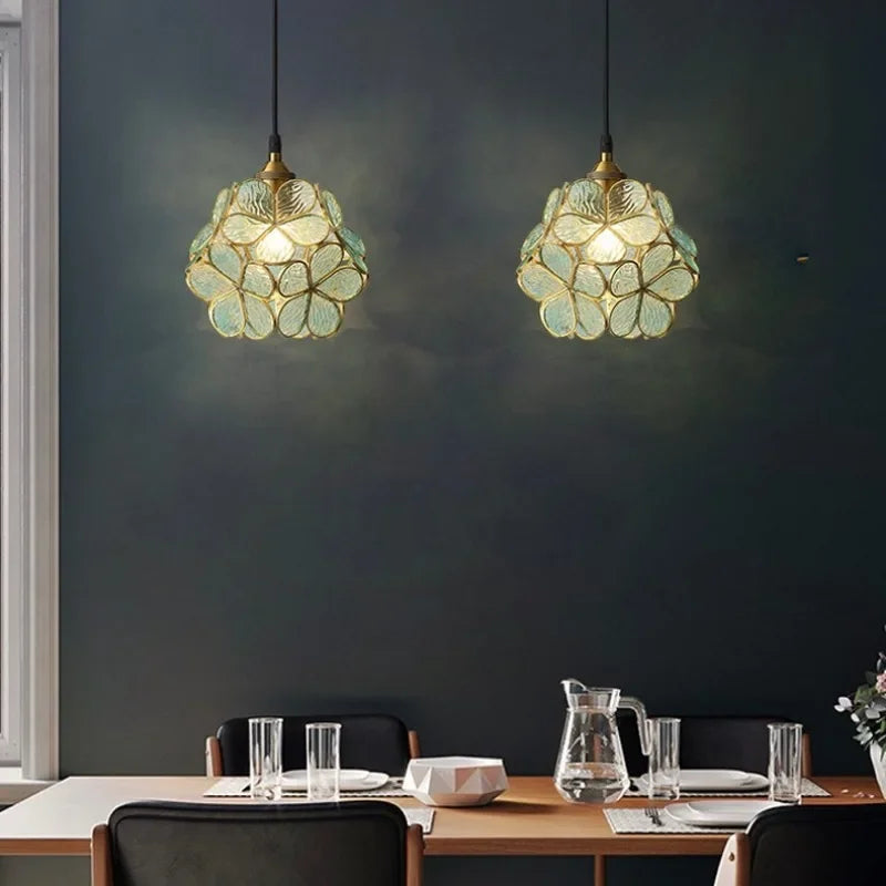 Two elegant translucent green petal acrylic pendant lights with gold metal accents hang symmetrically above a dining table