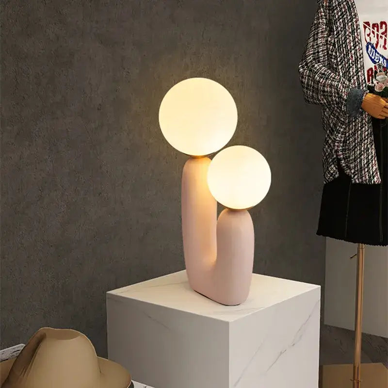Pastel pink ceramic ball table lamp with two glowing spherical bulbs for bedroom decor in nordic style