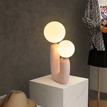 Pastel pink ceramic ball table lamp with two glowing spherical bulbs for bedroom decor in nordic style