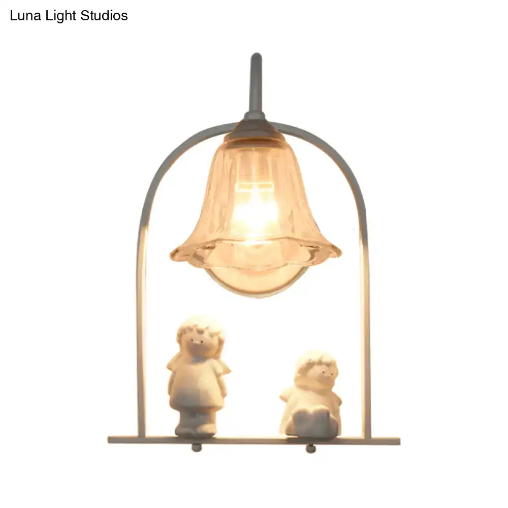 Warm-toned bell-shaped glass lamp with metallic frame and white arched frame casting light on ceramic figurines
