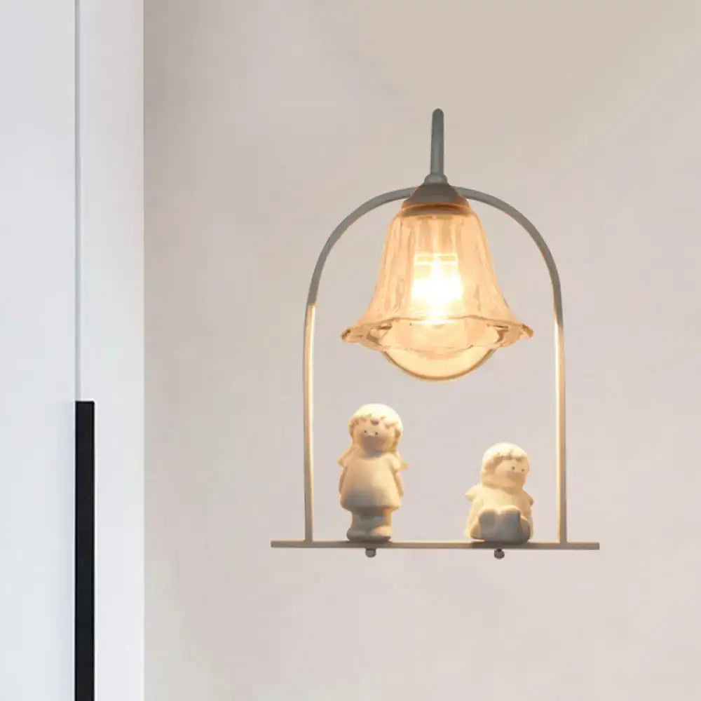 A warm-toned glass bell pendant light with a white arched frame metal structure and ceramic figurines beneath for bedroom decor