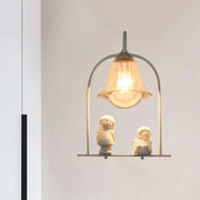 A warm-toned glass bell pendant light with a white arched frame metal structure and ceramic figurines beneath for bedroom decor