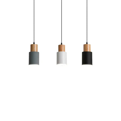 Three minimalist pendant lights with solid wood tops and cylindrical shades in gray white and black for kitchen use