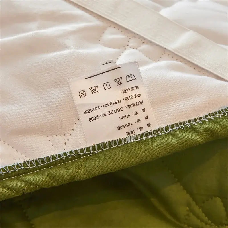 Cream-colored quilted bed skirt set with green border white stitching and 100% cotton label for bedroom use