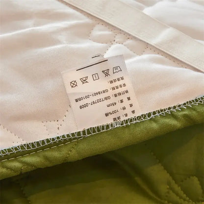 Cream-colored quilted bed skirt set with green border white stitching and 100% cotton label for bedroom use