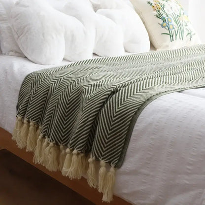 A soft olive green and cream decorbites geometric knitted blanket with herringbone pattern and fringed tassels for living room decor