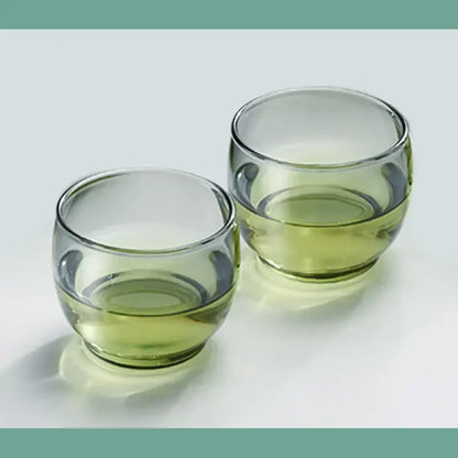 Two clear olive green glass tea cups filled with light green liquid in a decorbites glass tea cup set for kung fu tea