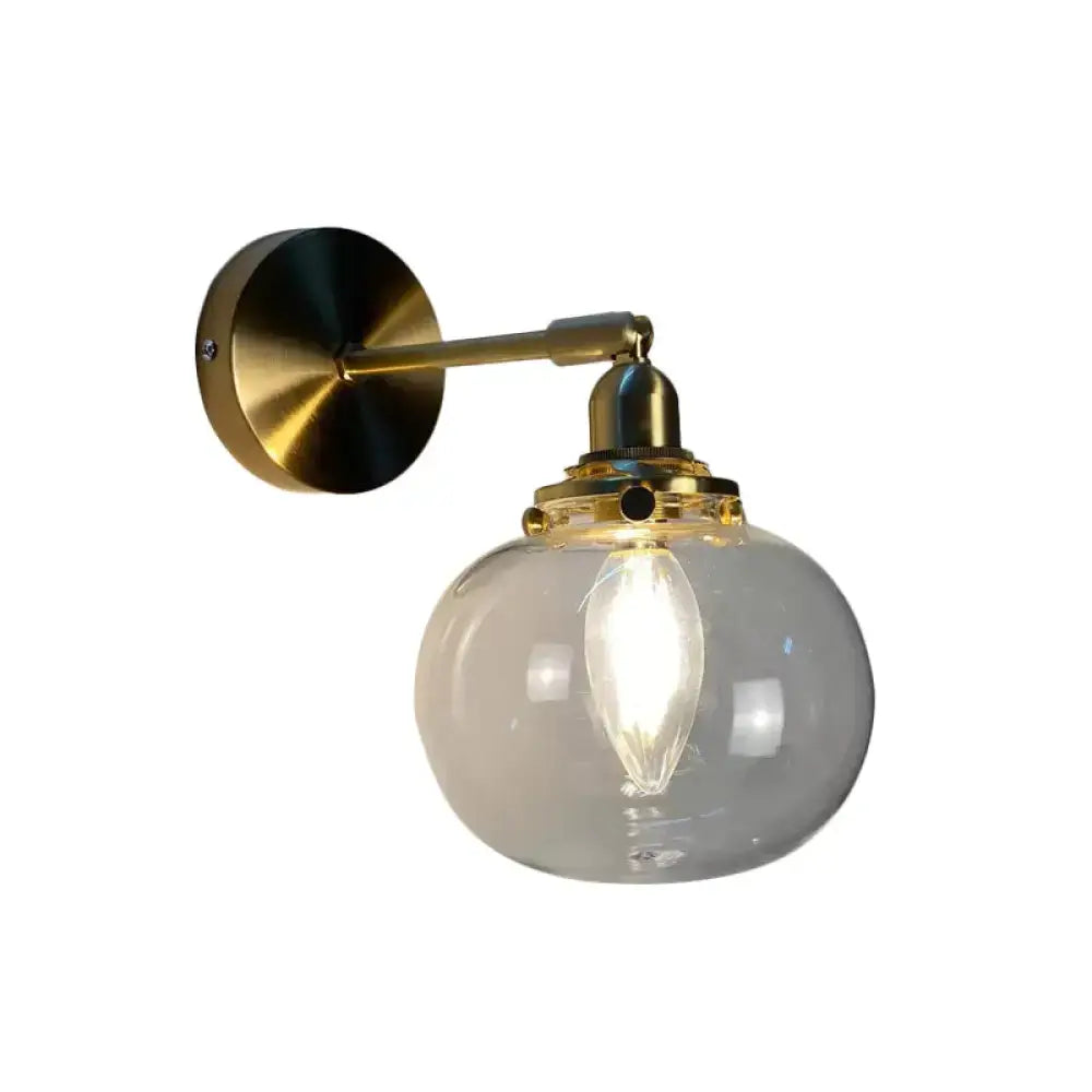Vintage-style bedroom wall lamp with brass arm and clear glass globe featuring an exposed filament bulb