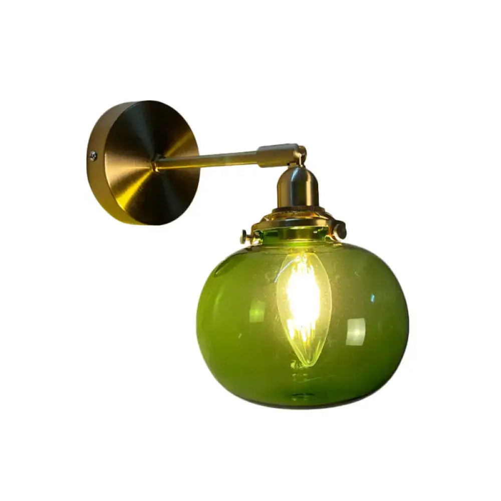 A vintage bedroom wall lamp with a brass metal arm and green glass globe featuring an illuminated filament bulb