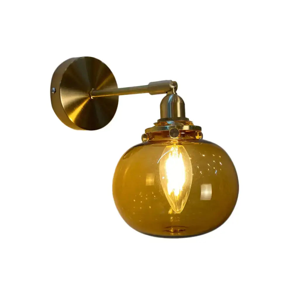 A warm amber glass globe wall lamp with brass-finished arm and mounting plate for bedroom wall lighting
