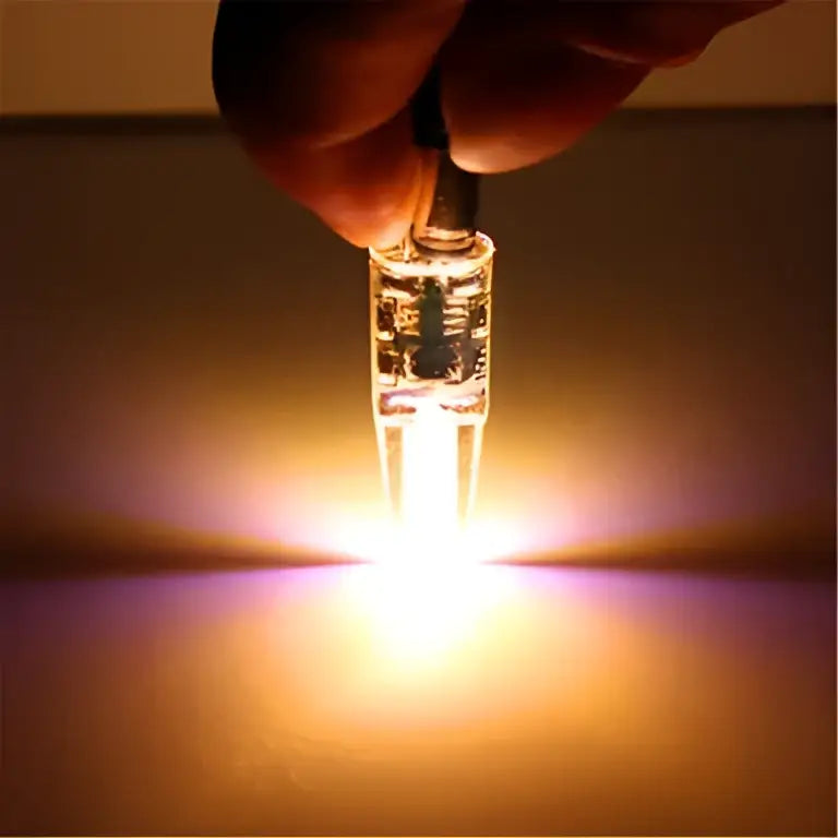 A hand holds a glowing clear glass orange decorbites g4 led bulb 220v cob light for living room pack of 10