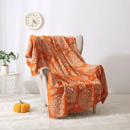 Orange paisley-patterned throw blanket with cream accents draped on chair featuring decorbites cashew pattern