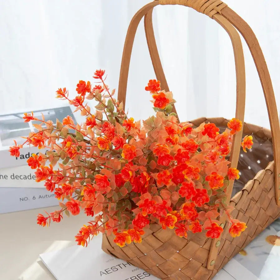 A vibrant orange and yellow artificial eucalyptus leaves arrangement in a woven wicker basket for garden decor