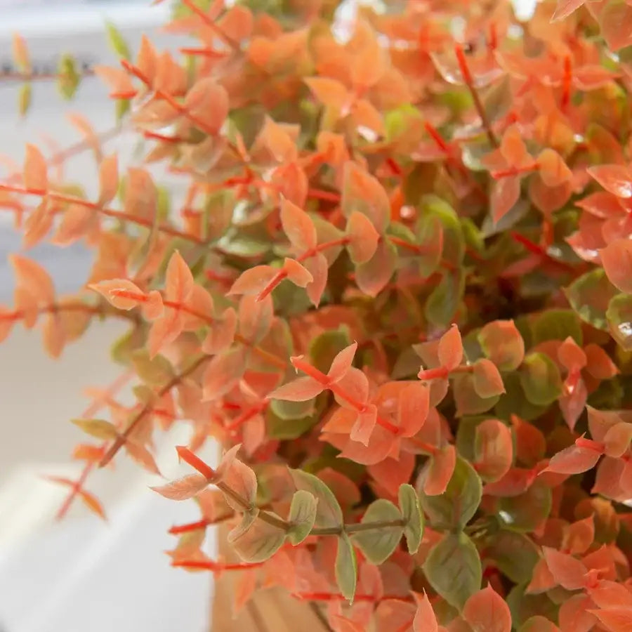 Orange and red artificial eucalyptus leaves with coral-pink and green stems in white pitcher for garden decor