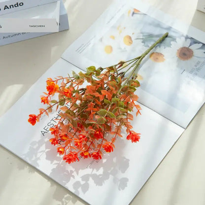A vibrant orange artificial eucalyptus flower bouquet with green leaves in a white pitcher for garden decor