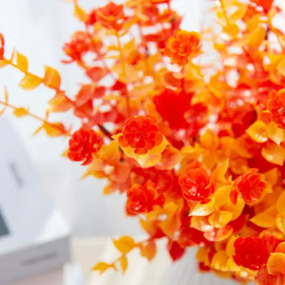 Orange and red artificial eucalyptus leaves with glossy plastic petals in white pitcher for garden decor