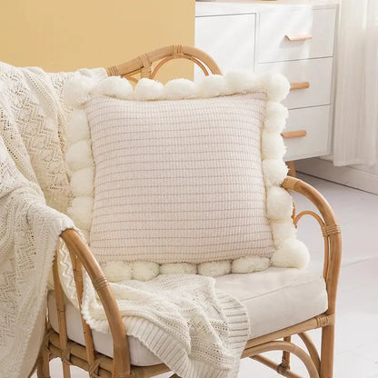 Cream-colored woven ball cushion cover with fluffy white pom-pom trim for living room decor