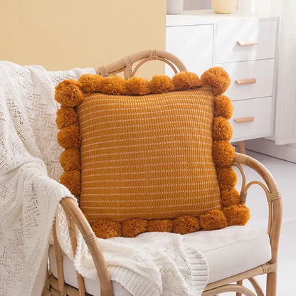 Warm amber orange textured ball cushion cover with woven fabric and decorative pom-poms for living room decor