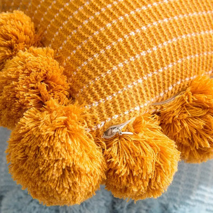Warm mustard-yellow knit ball cushion cover with white grid pattern and fluffy pom-poms for living room decor