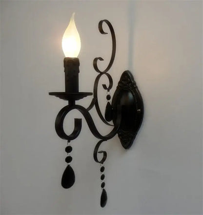 Ornate black wrought iron wall lamp with scrollwork and teardrop crystals featuring a candle-style bulb for living room decorbites black wrought design