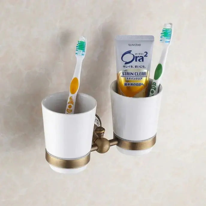 Ornate brass and white ceramic bath hardware set featuring a dual cup toothbrush holder with gold toned accents