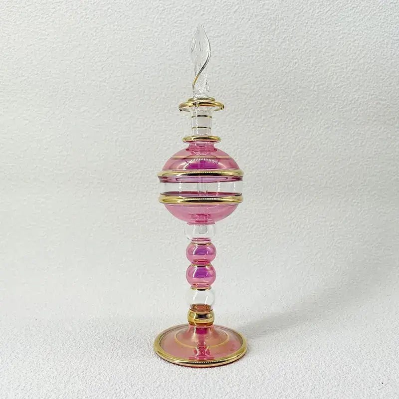 A delicate pink and clear glass bottle jewelry ornament with gold bands and an ornate stopper for bedroom decor