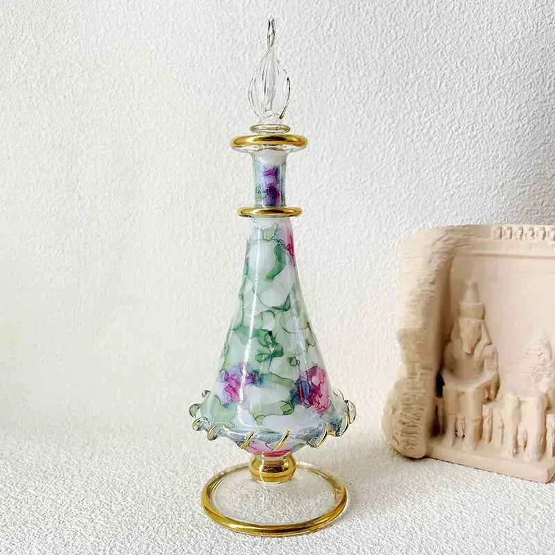 A delicate glass bottle jewelry ornament with a fluted base gold accents and hand-painted pink green florals