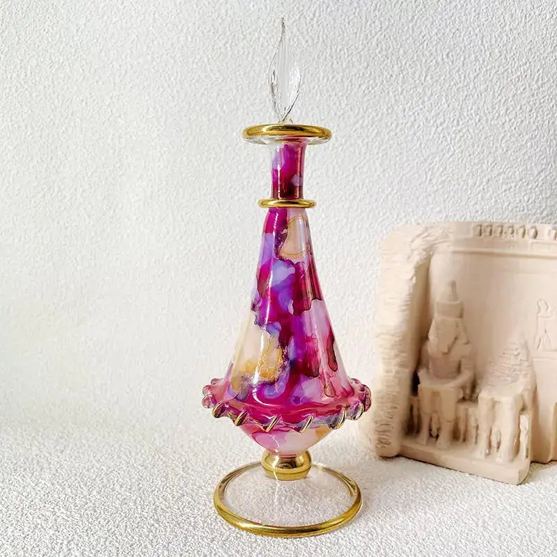 A vibrant hand-blown glass bottle with magenta and purple hues and gold accents used as bottle jewelry ornaments