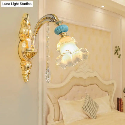 Ornate gold-toned wall mount light with blue and clear glass lampshade crystal pendant and decorative leaf motifs
