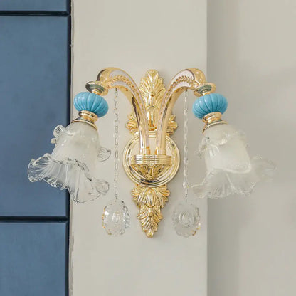 Ornate gold-toned wall mount light with two frosted glass shades, turquoise ceramic knobs, and crystal pendants for bedroom use