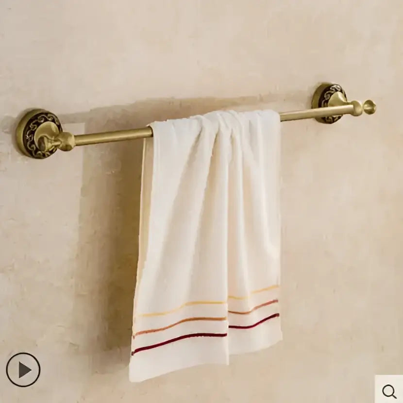 Ornate gold copper carved bathroom accessories set with brass towel rack holding white towel with gold orange and burgundy stripes