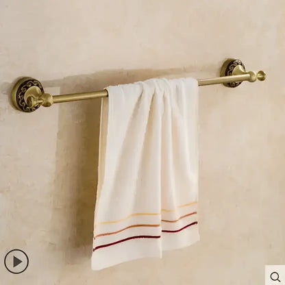 Ornate gold copper carved bathroom accessories set with brass towel rack holding white towel with gold orange and burgundy stripes