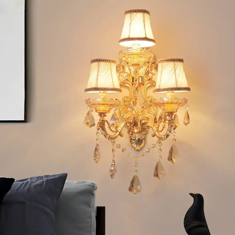 Ornate gold metal fixture living room sconce with three cream fabric shades and crystal teardrop accents 20 inch fixture