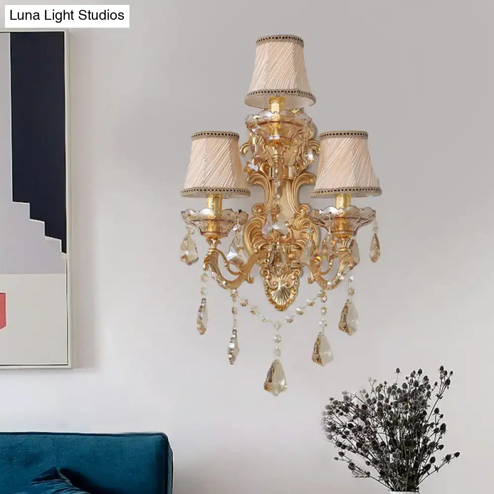 Ornate gold metal fixture 3 light wall sconce with crystal droplets and cream fabric shades perfect for living room use