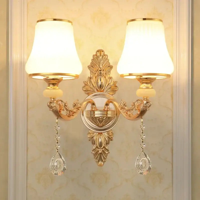 Ornate gold-finished crystal wall sconce with two cream fabric shades and dangling teardrop pendants for bedroom decorbites wall sconce