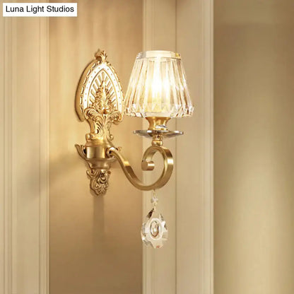 Ornate gold-toned wall sconce contemporary with faceted crystal shade and dangling crystal pendant for bedroom lighting