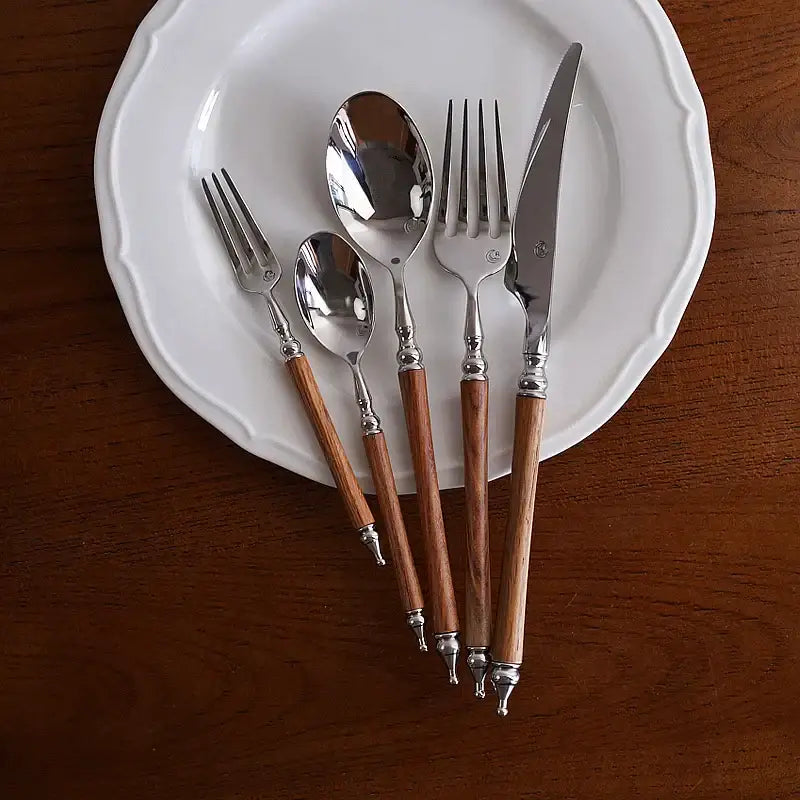 Ornate silver and wood stainless steel tableware set with polished metal heads and decorative wooden handles for dining room