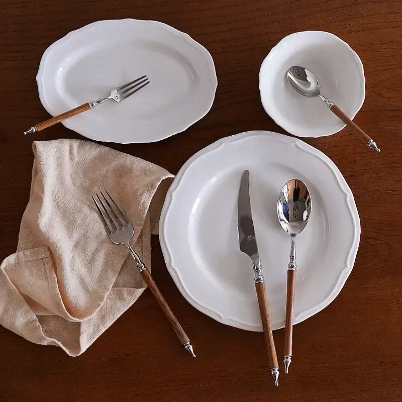 White ceramic plates with scalloped edges and a stainless steel western tableware set featuring ornate silver and wood handles