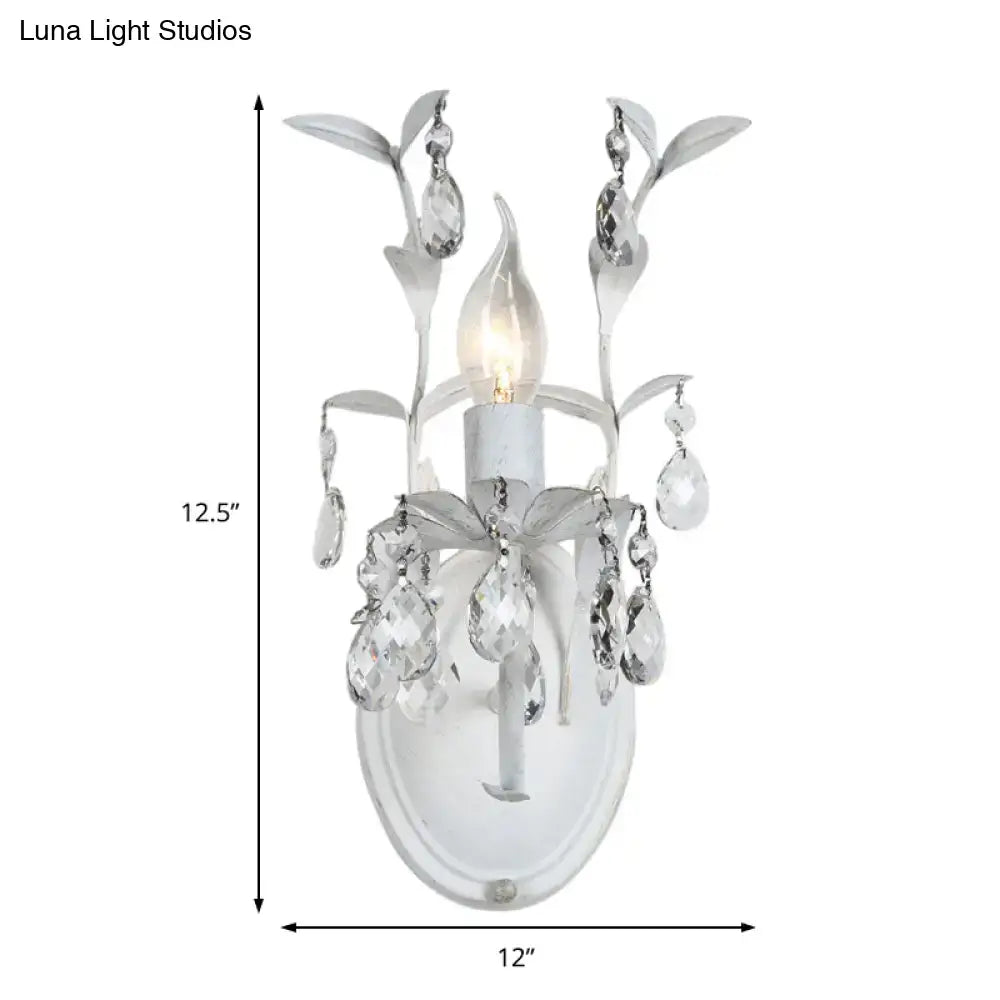 Ornate white metal wall light fixture with silver crystal leaf and teardrop accents for bedroom sconce lighting