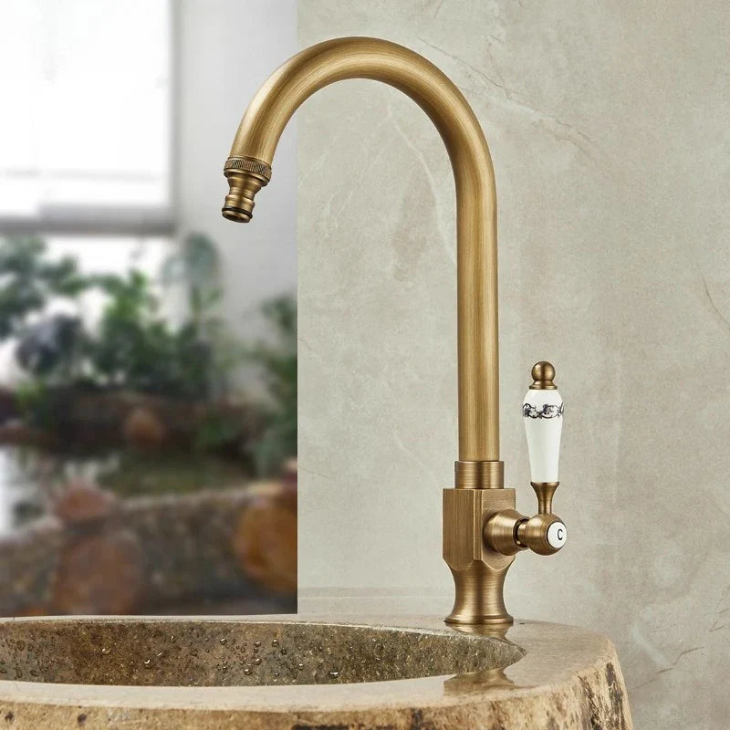 Antique brass single hole outdoor antifreeze faucet with curved spout and ornate white ceramic handle with black detailing