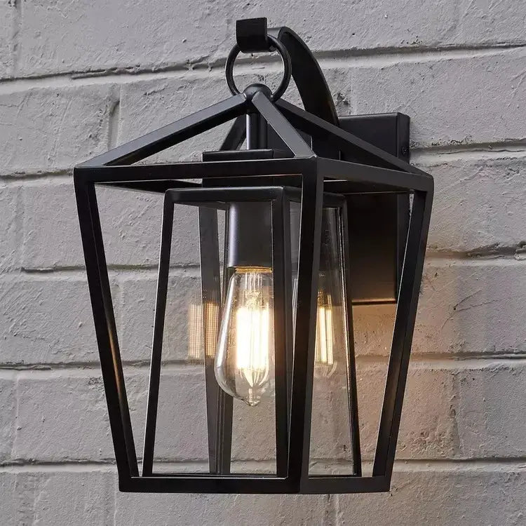 Black wrought iron outdoor wall light with glass shades and an exposed filament bulb for outdoor use