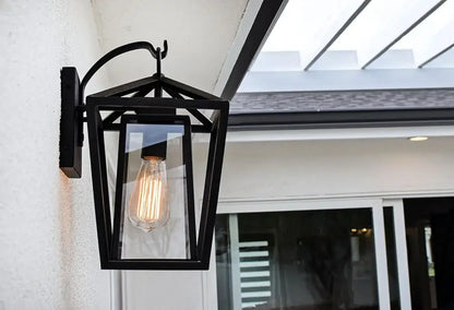 Black wrought iron outdoor wall light with glass shades housing glowing filament bulb for waterproof use