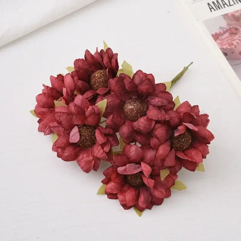 Cluster of artificial maroon paper flowers with glittery brown centers and green leaves in decorbites daisy sunflower bouquet