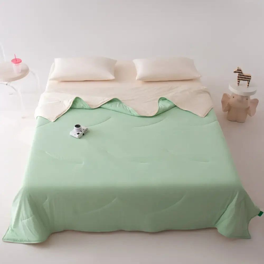 A pastel green summer cooling comforter with quilted texture and cream underside, ideal for decorbites green summer bedding