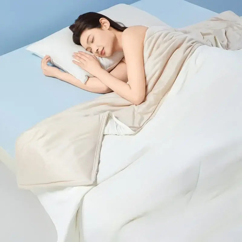 A woman sleeps peacefully under a cream-colored duvet on a light blue bed with decorbites green summer cooling comforter
