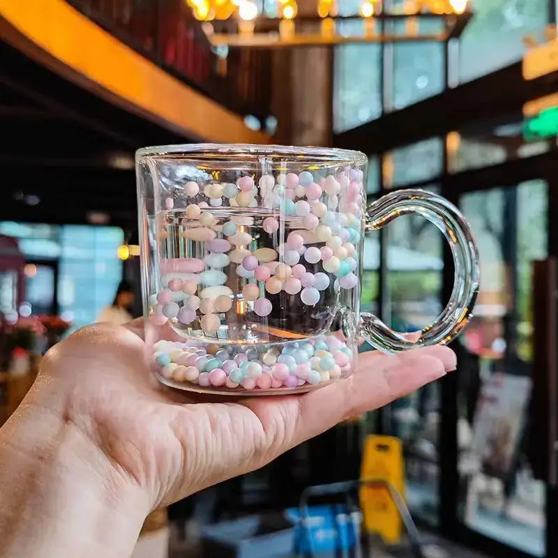 A clear double wall glass cup filled with pastel heart bubble quicksand beads for dining room use